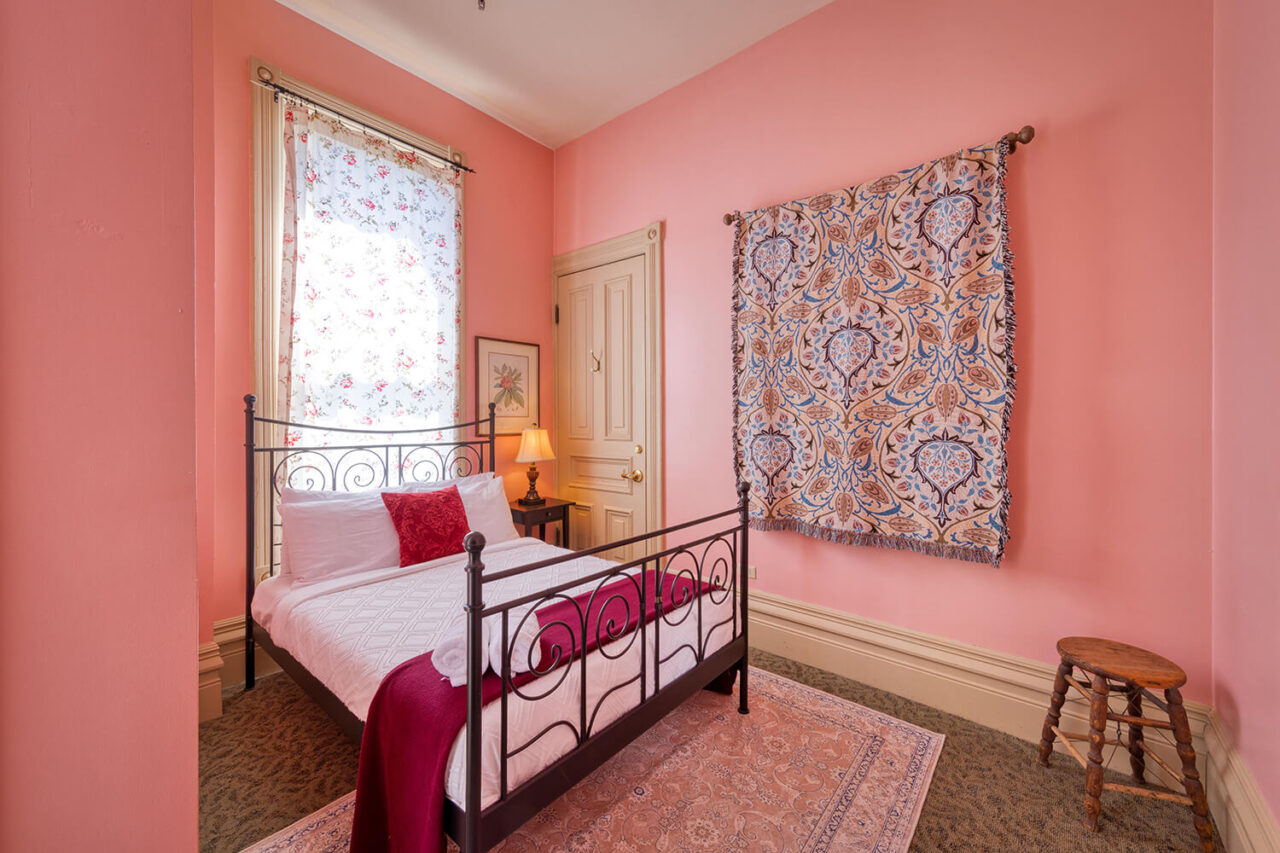 a private double room at HI Sacramento hostel with one full-sized bed, pastel walls, hanging tapestries, and windows letting in natural light.