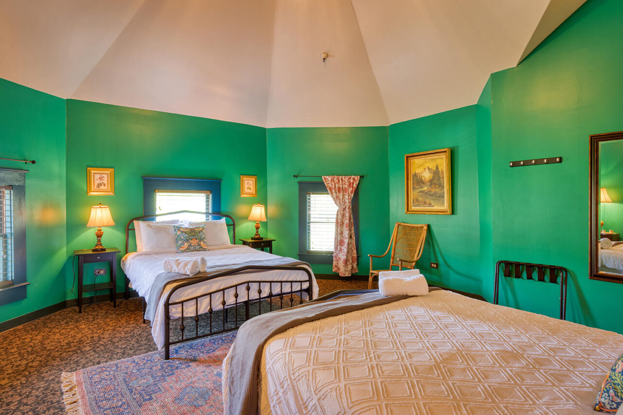 a private room at HI Sacramento with high ceilings, two queen-sized beds, and emerald green walls