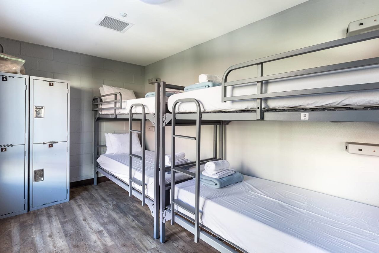 four bunk beds with fresh linens in a well lit room with storage lockers