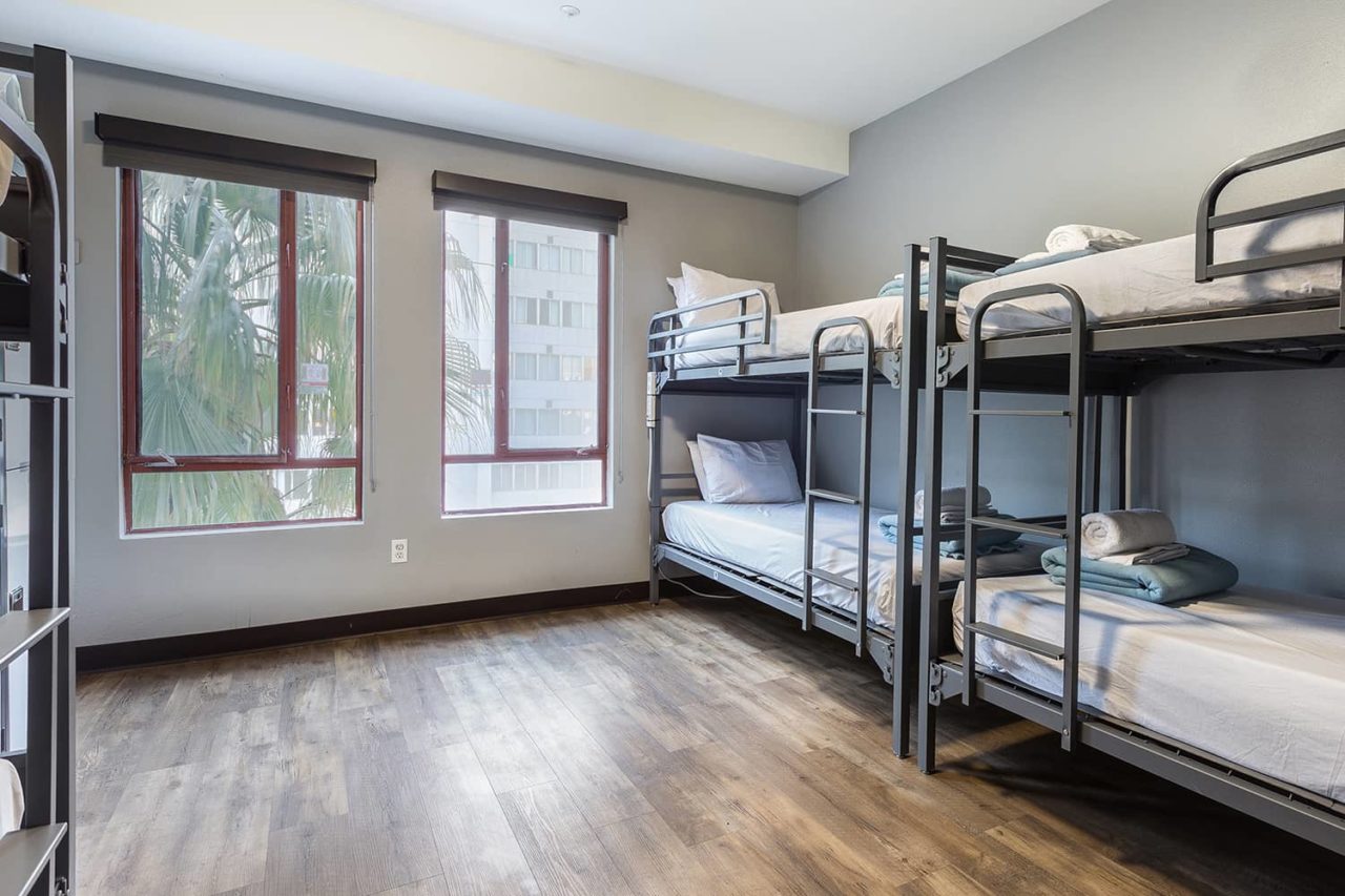 a large dorm room with four sets of bunk beds and wood flooring with big window