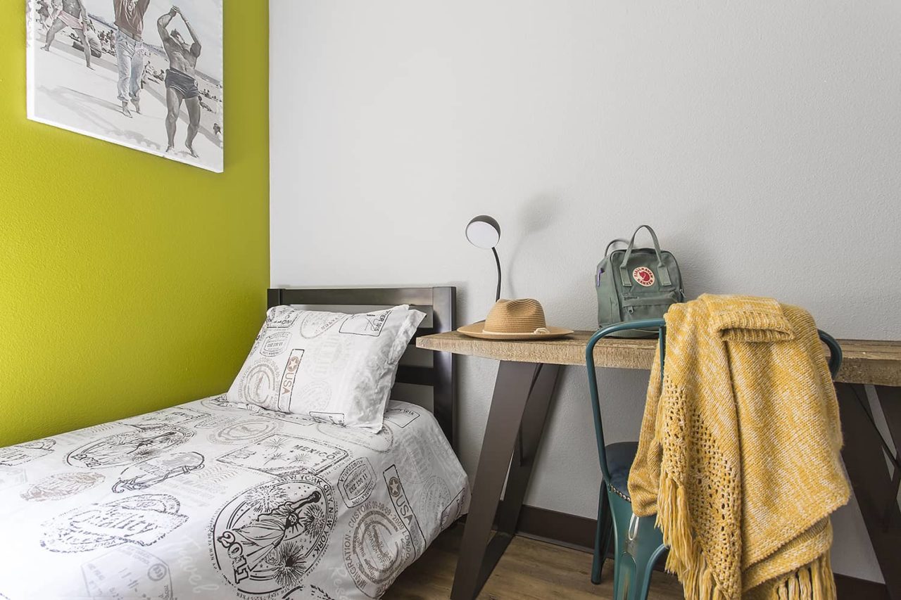 a freshly made twin bed next to a desk with chair and lamp inside a small private room at Hi Los Angeles Santa Monica hostel