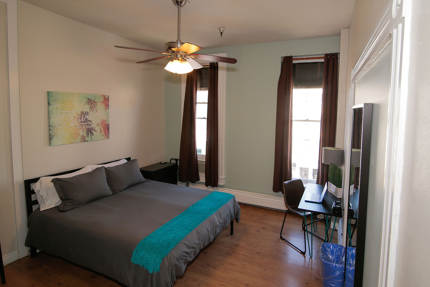 A private room at HI San Diego Downtown hostel with a freshly made queen-sized bed, two windows, and a desk and chair.