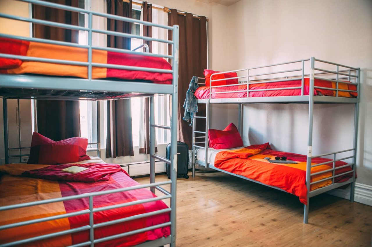 four bunk beds with red and orange bedspreads in a room with wood floors