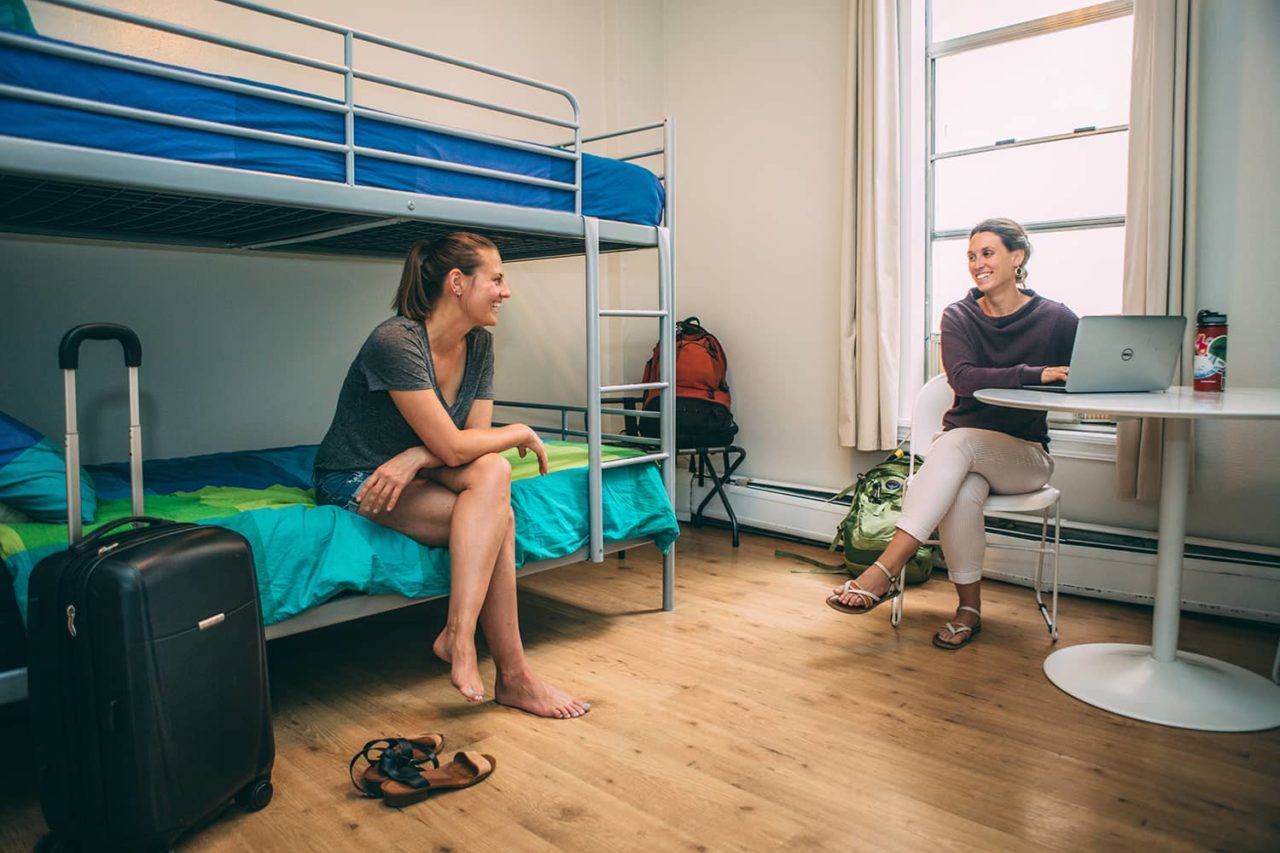 two women sit talking in a room with bunk beds and a table at HI San Diego Downtown hostel