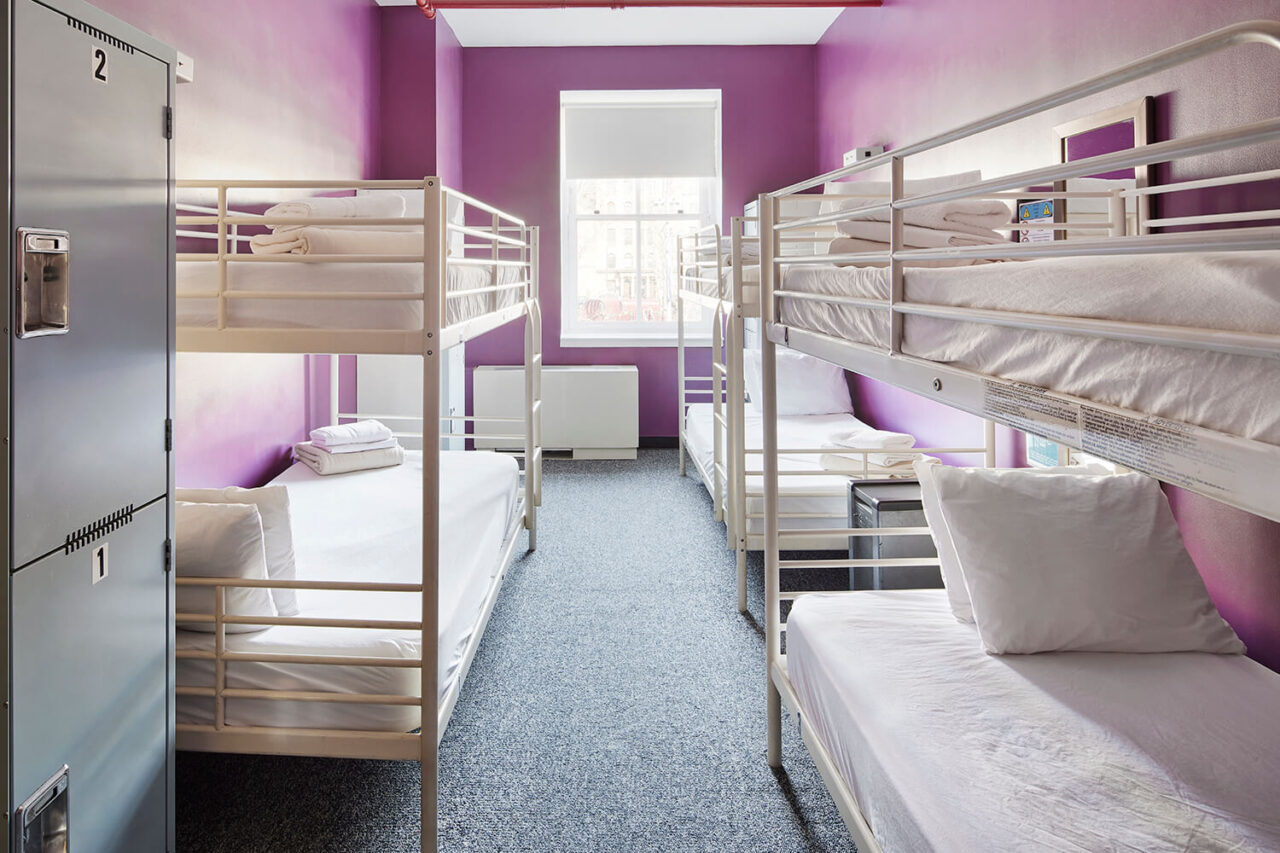 three sets of freshly made bunk beds with clean white linens in a dorm room with purple walls at HI New York City hostel