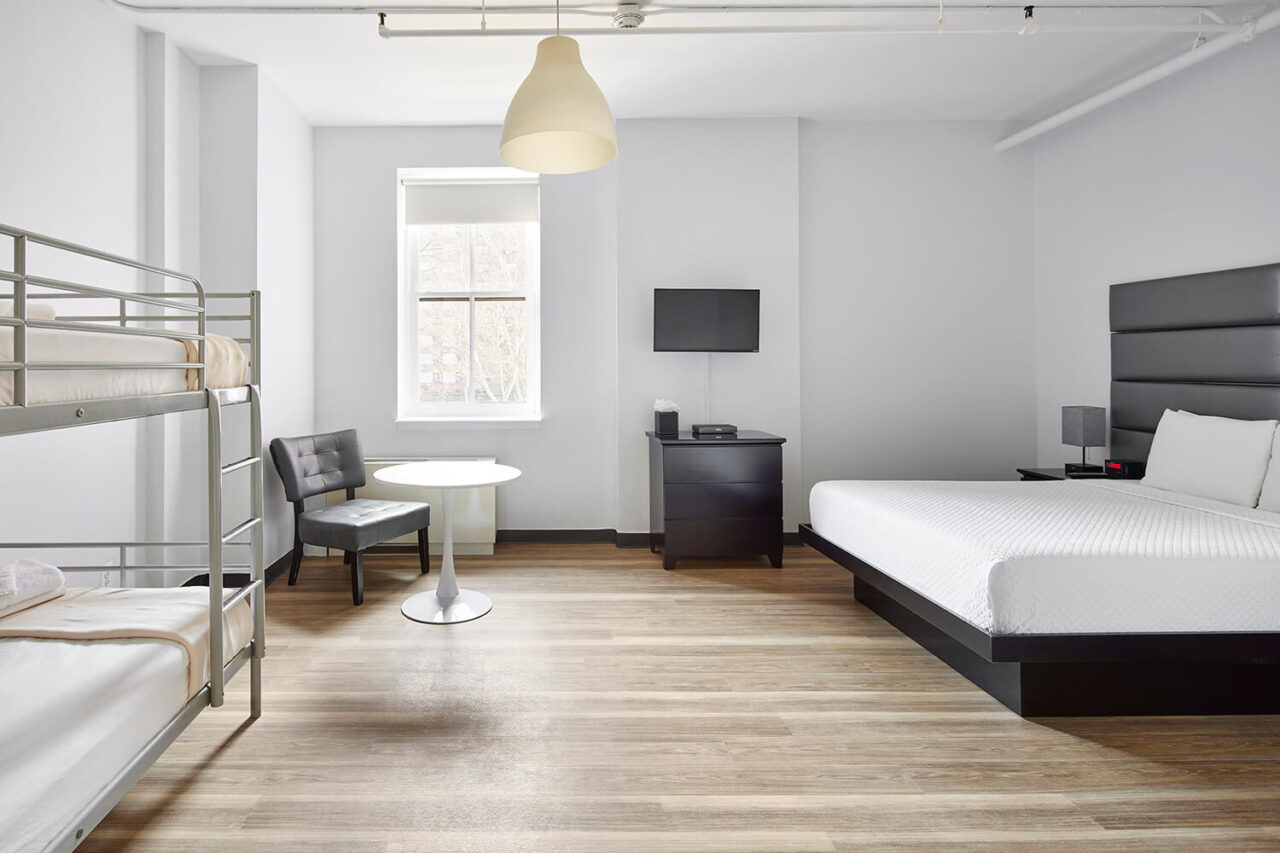 a large ensuite private room at HI New York City hostel with one freshly made king-sized bed, one set of twin-sized bunk beds, a table with chairs, a mini fridge, and a TV.