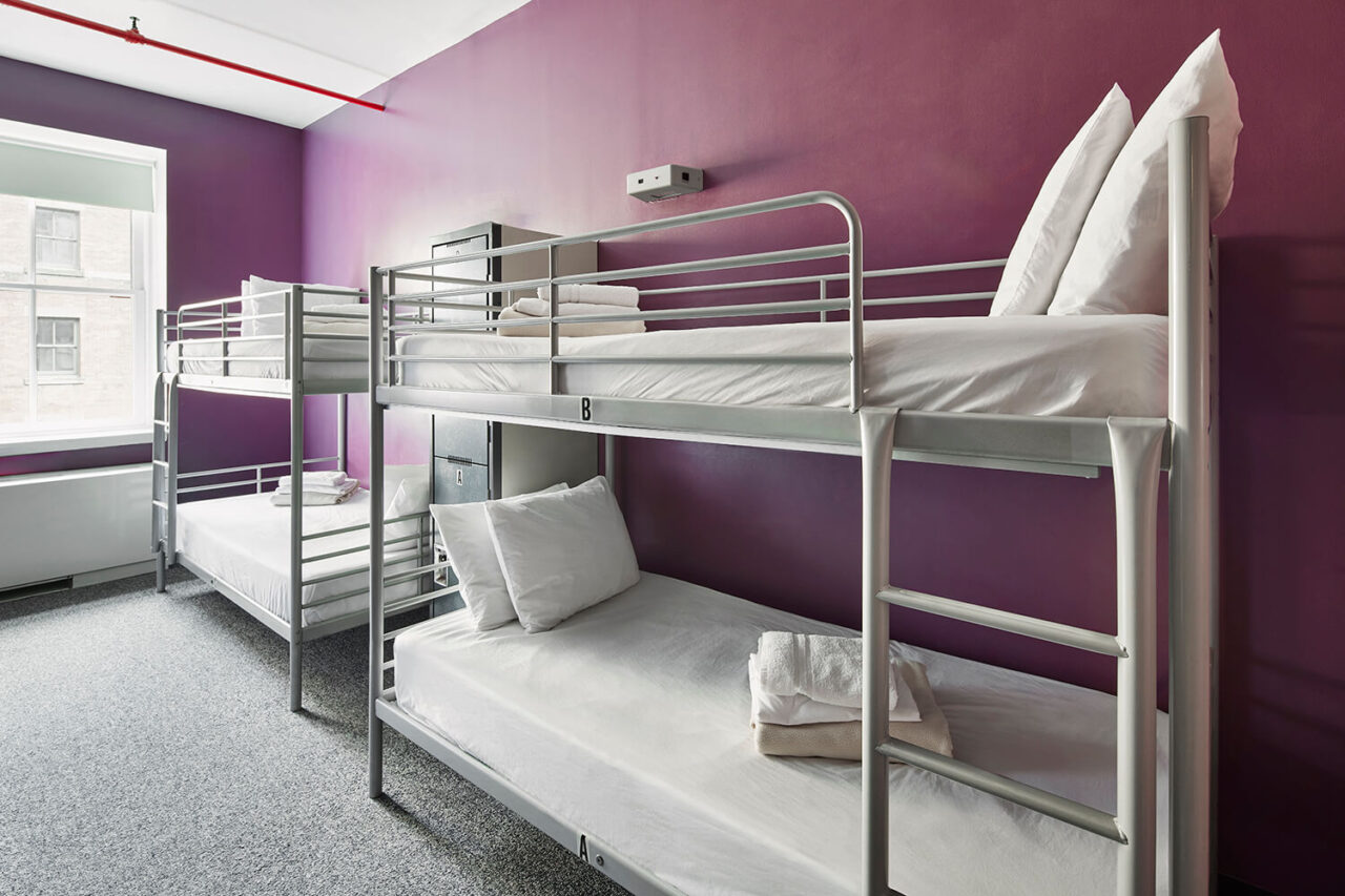 two sets of freshly made twin-sized bunk beds in a spacious dorm room with purple walls at HI New York City hostel