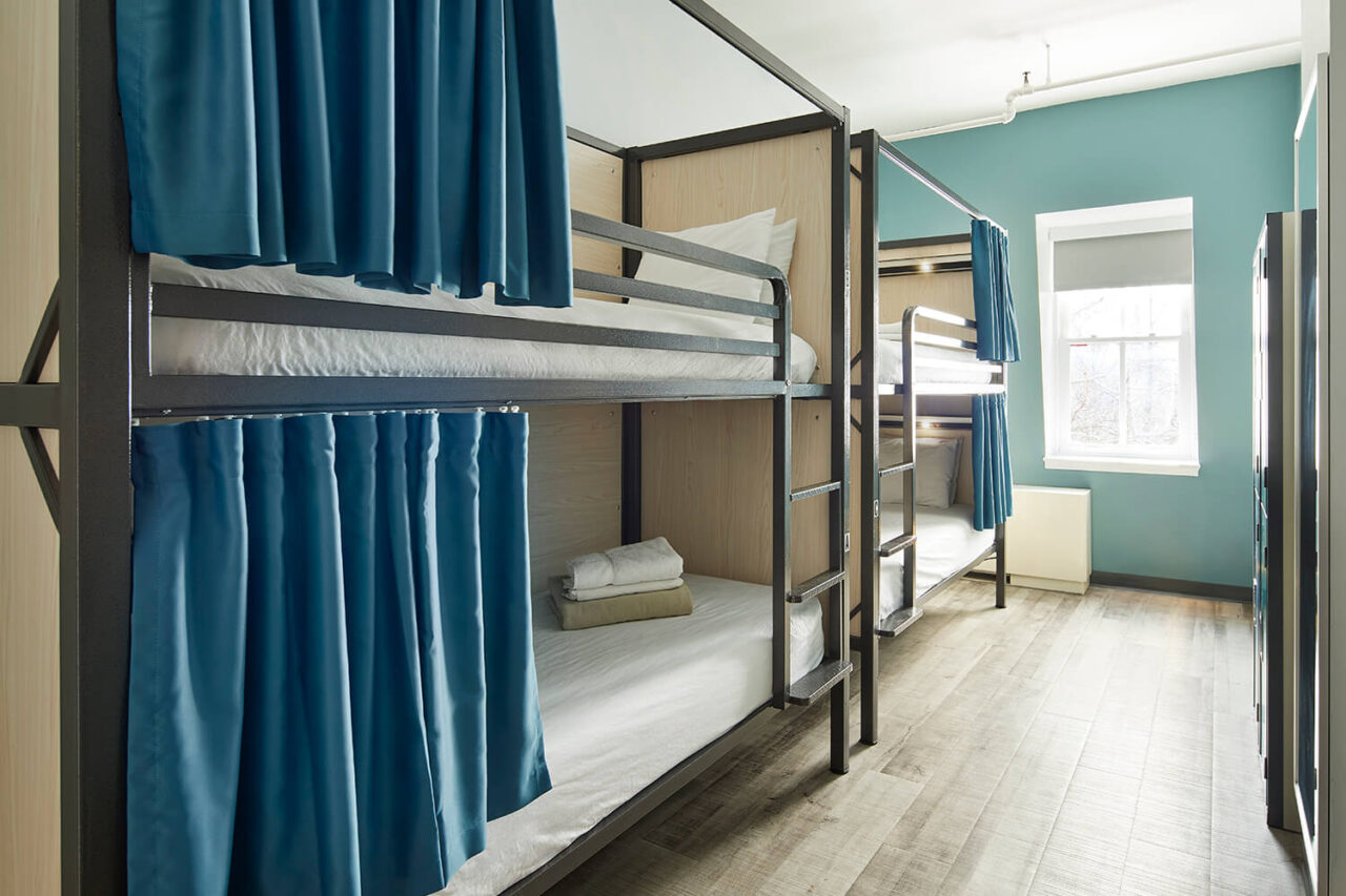 two sets of new bunk beds with privacy screens, privacy curtains, reading lights, and USB charging ports in a well lit dorm room at HI New York City hostel.