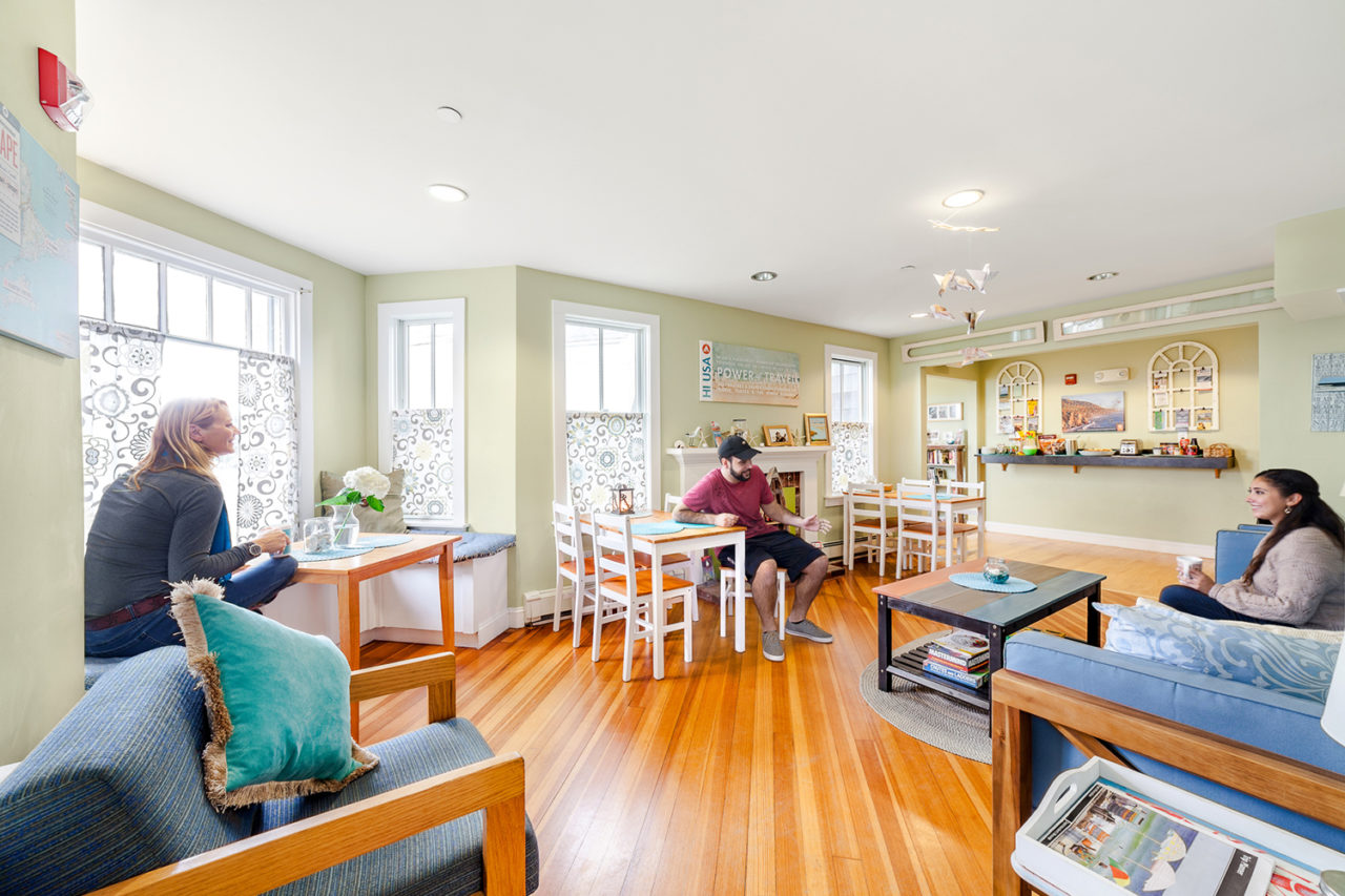 three people sit talking in a bright and airy guest lounge at HI Hyannis hostel