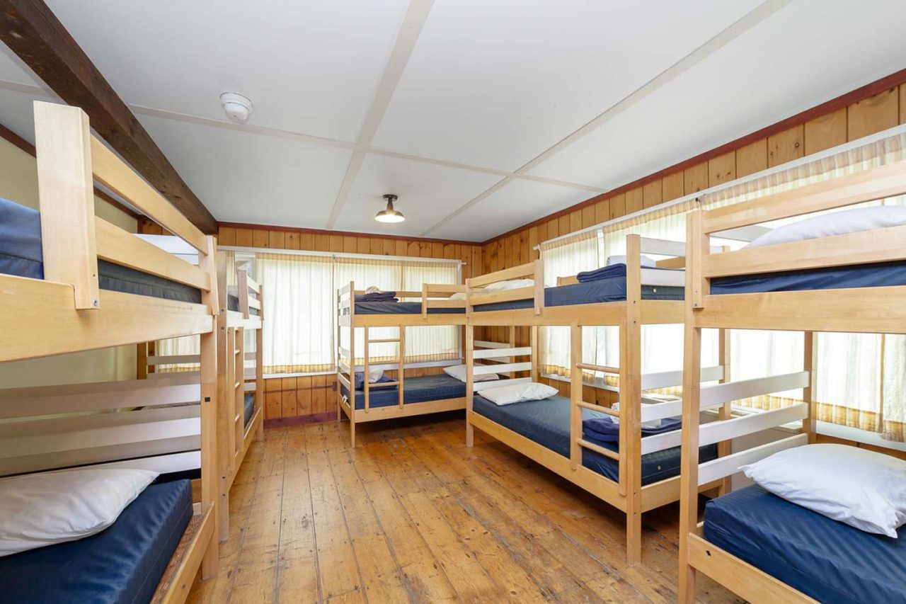 a dorm room at HI Martha's Vineyard hostel with five sets of twin-sized bunk beds. There are hardwood floors, wood-paneled walls, and lots of windows letting in natural light.