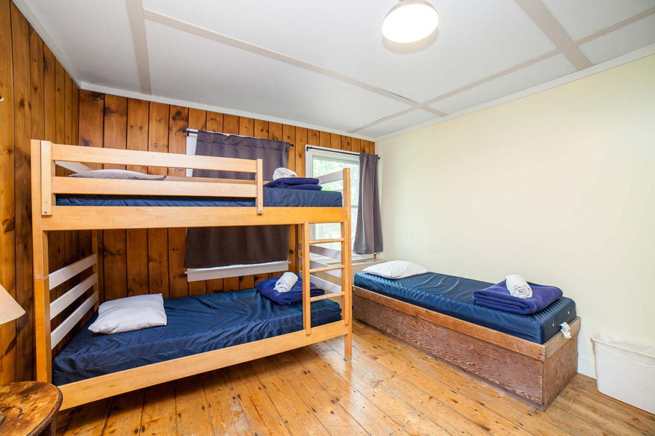 a bedroom at HI Martha's Vineyard hostel with hardwood floors and wood paneling on the walls, with one set of twin-sized bunk beds and one single twin-sized bed