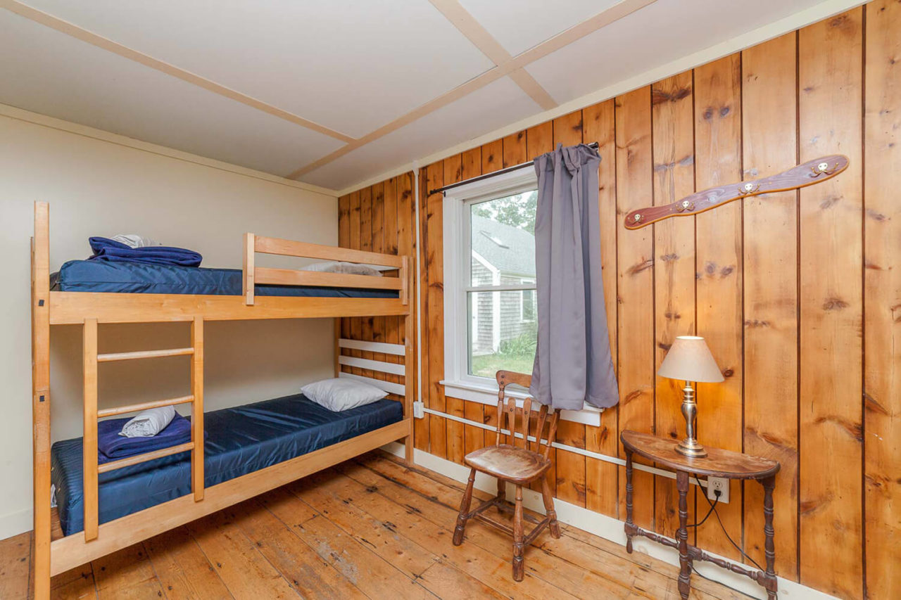 one set of bunk beds, a stool, and small table with lamp in a wood-paneled room
