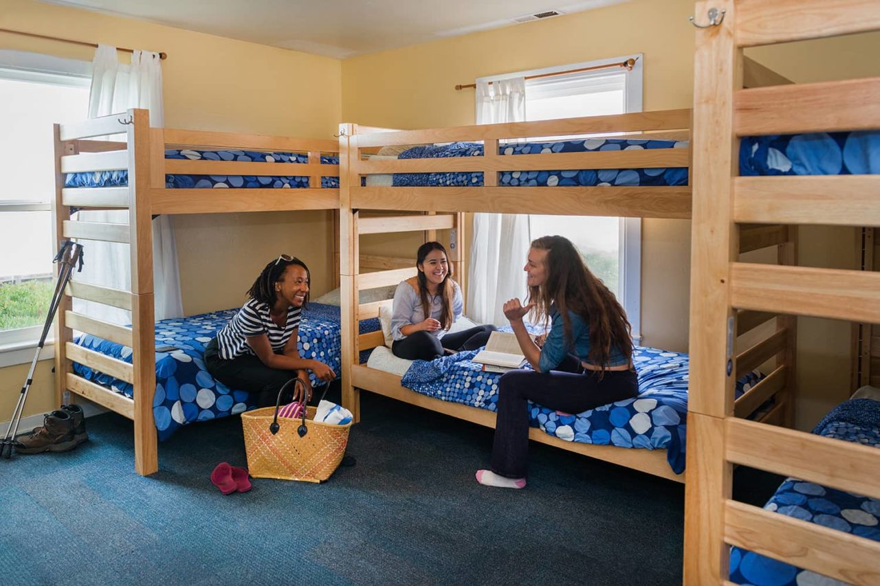 three women sitting on bunk beds with blue bedspreads