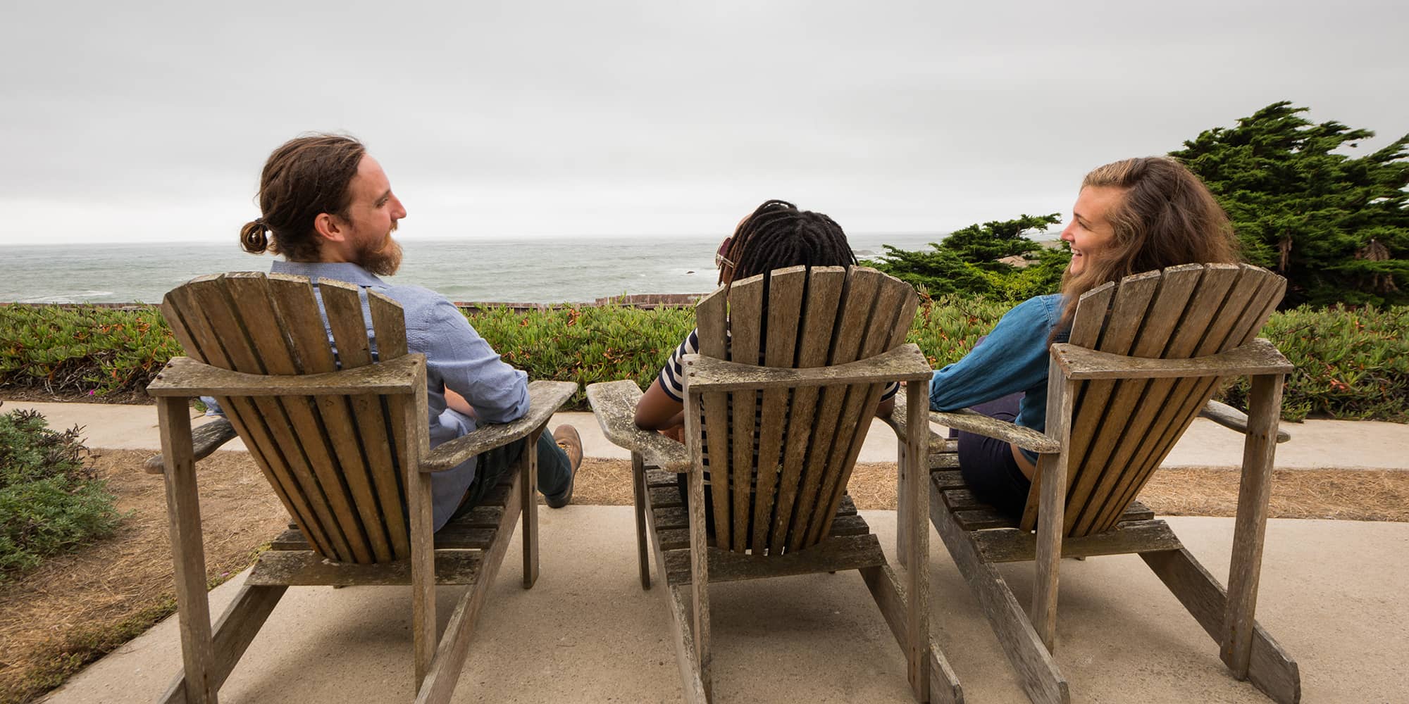 three people sit in adirondak chairs overlooking the ocean at HI Pigeon Point Lighthouse hostel