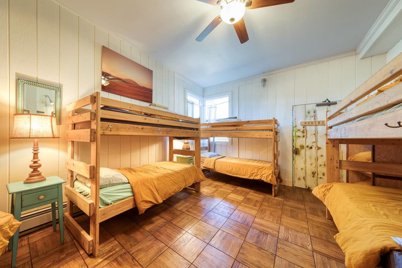 a brightly lit room with wood floors and three sets of twin bunk beds with yellow bedspreads