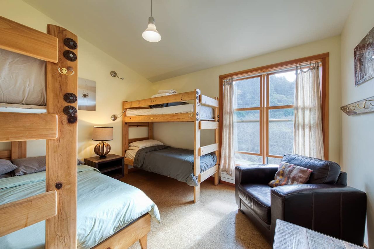 a light-filled room with one set of twin bunk beds, a full-sized bed with one bunked twin over it, and an armchair and table