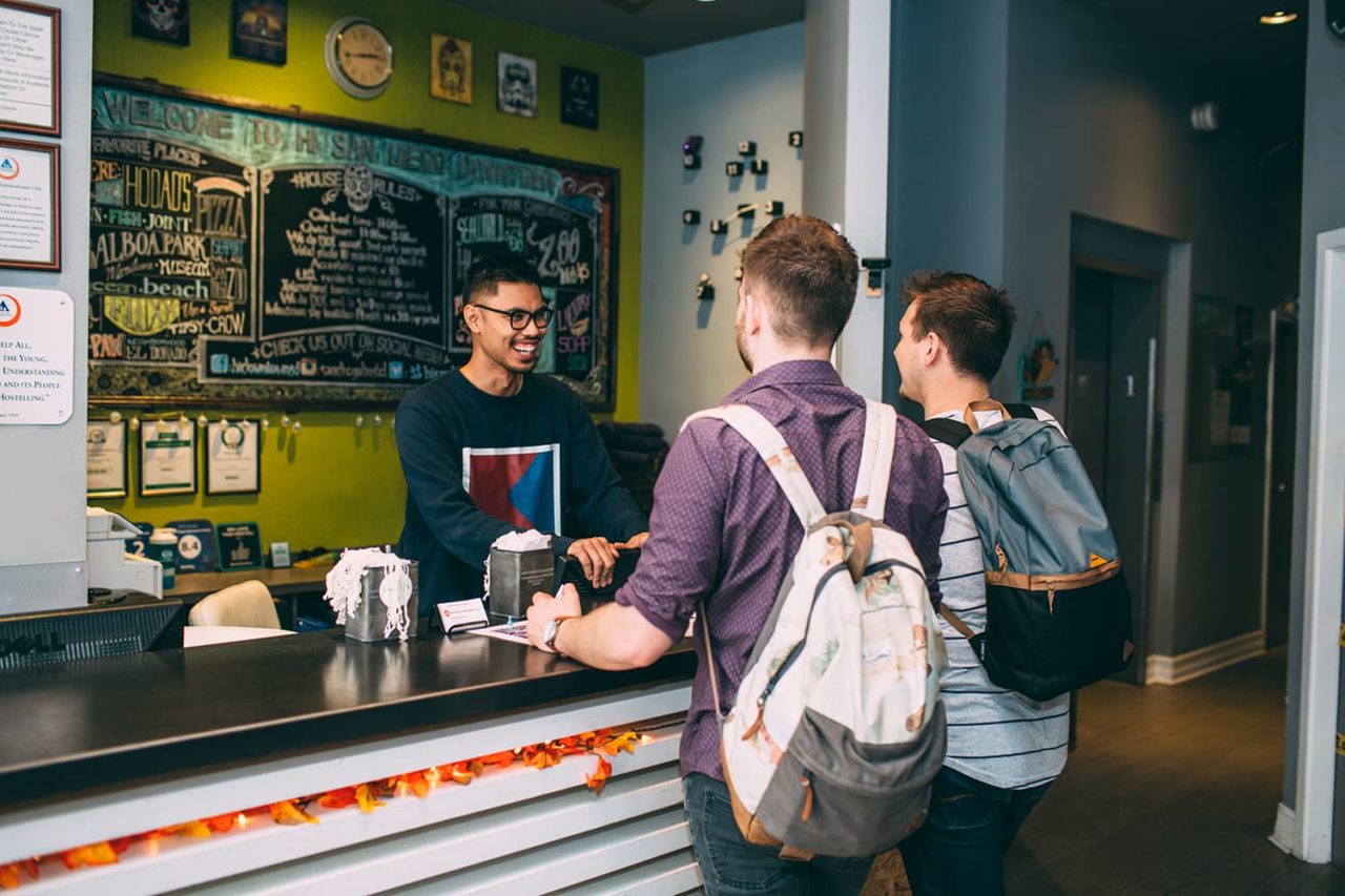 a friendly front desk agent at HI San Diego Downtown hostel checks in two guests at the front desk