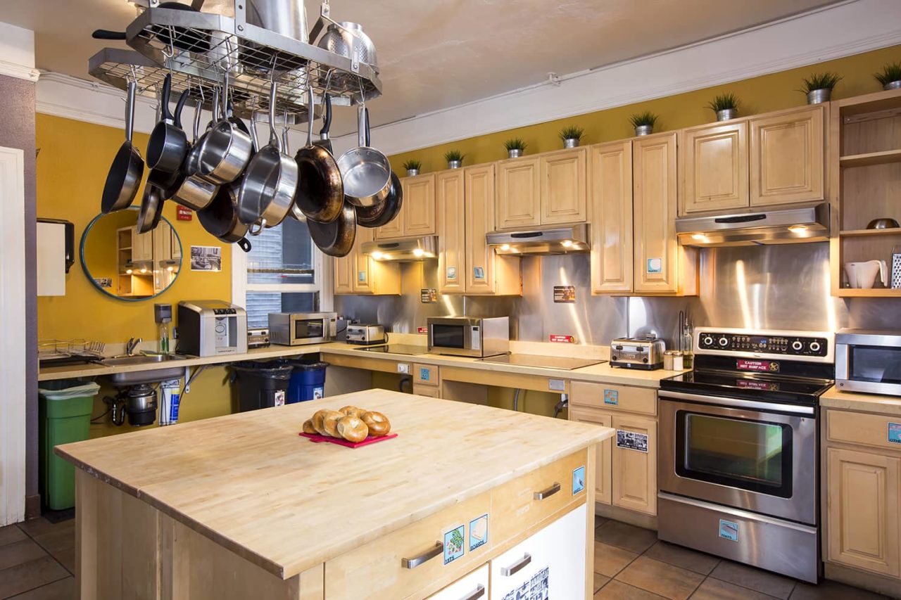 The guest kitchen at HI San Francisco Downtown Hostel, with a countertop with pans hanging above and a stove in the background