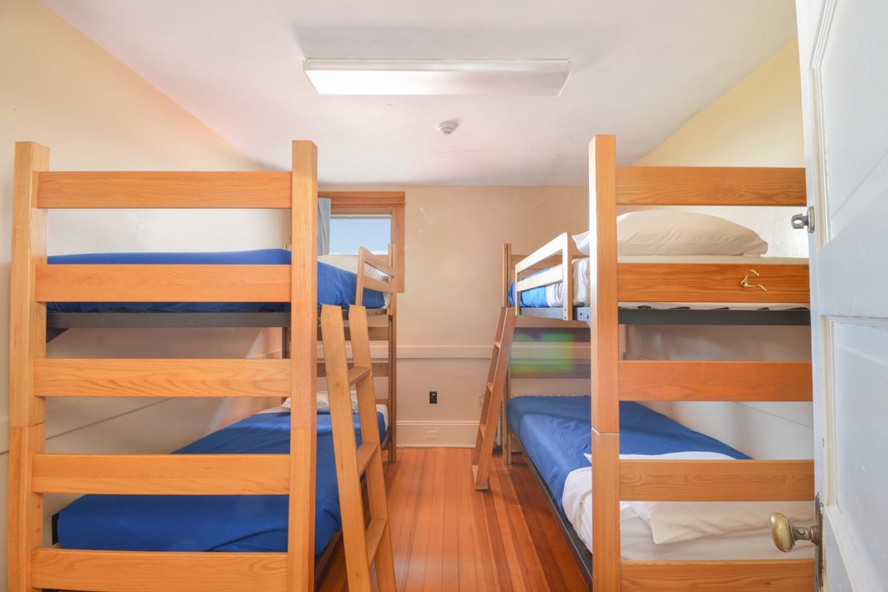 a small private room at HI Truro hostel on Cape Cod with four wooden bunk beds and a window looking out over the landscape.