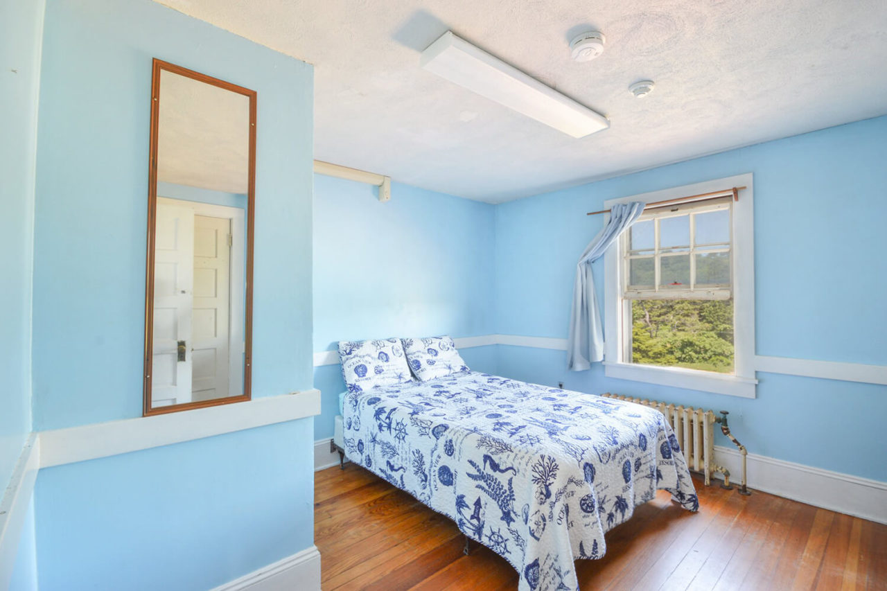a full-sized bed in an airy room with a view of the ocean out the window
