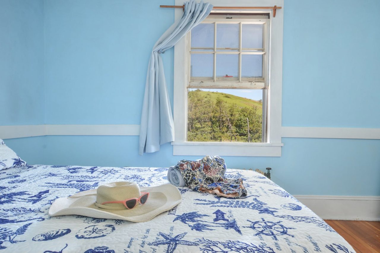 A private room at HI Truro hostel on Cape Cod. There is a full-sized bed with a blue-and-white bedspread and a window looking out over the landscape.