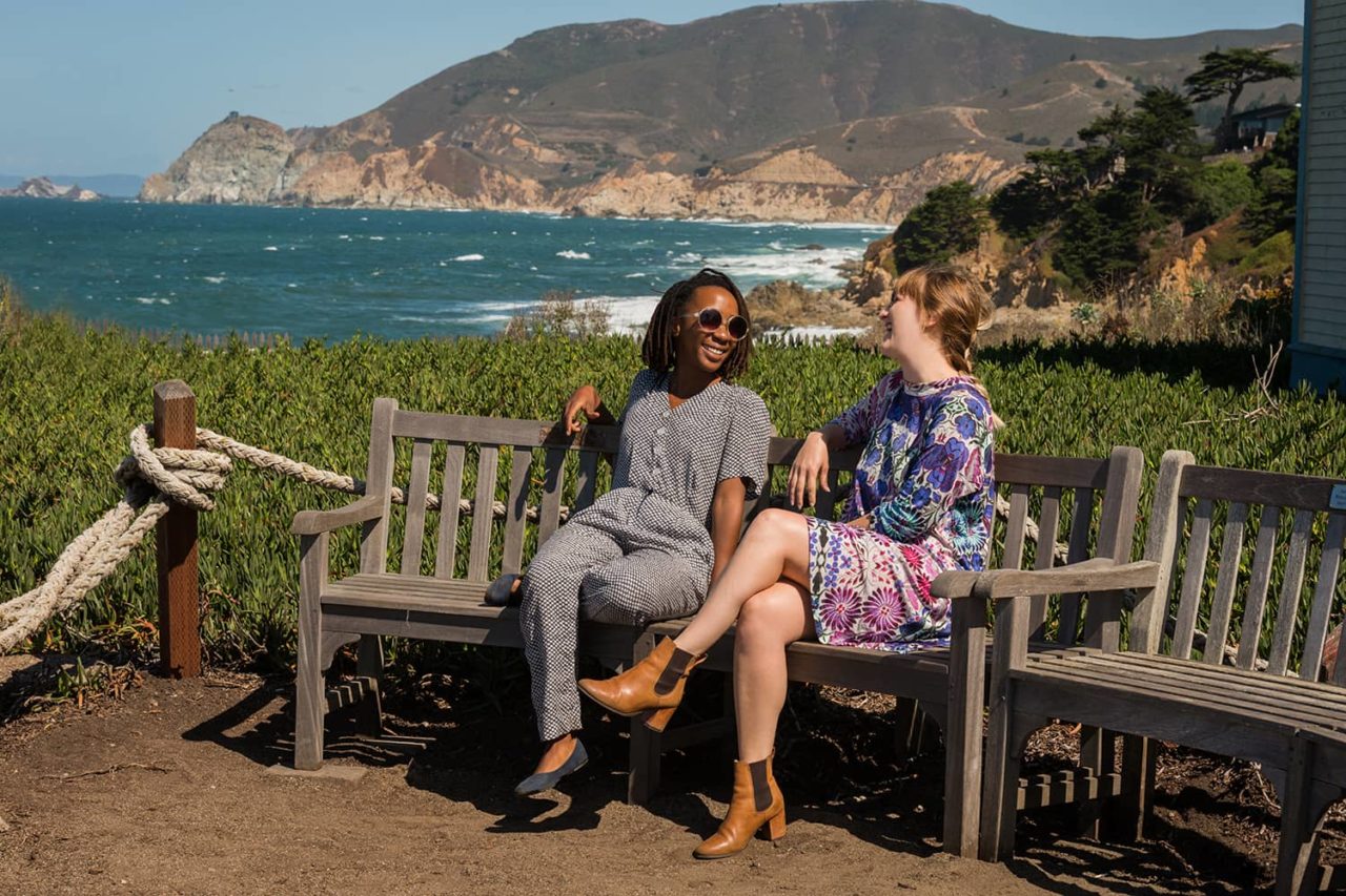 two women sit on a bench overlooking the pacific ocean