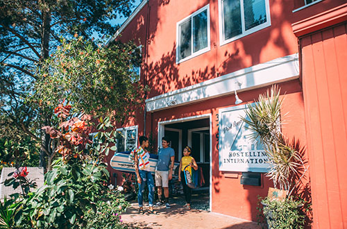 3 people with a surfboard in front of HI San Diego Point Loma hostel