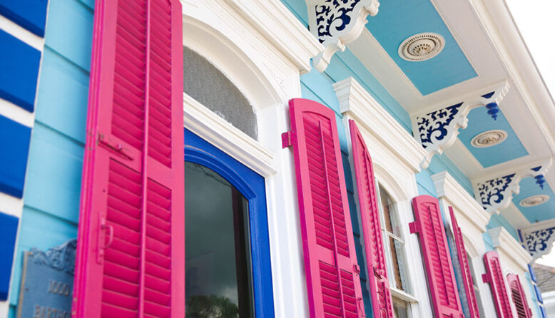 a close-up of a pale blue house with white molding and hot pink shutters in New Orleans LA