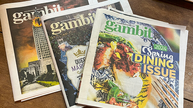 Three issues of New Orleans' Gambit spread out on a wood tabletop