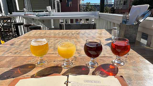 a flight of four different colorful beers in small tulip glasses sit on a wood table on the rooftop deck of Half Door Brewing in San Diego.