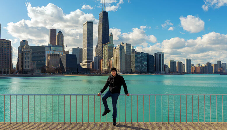 a young man poses in front of Lake Michigan overlooking the Chicago skyline
