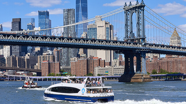 a NYC commuter ferry goes by the Manhattan bridge