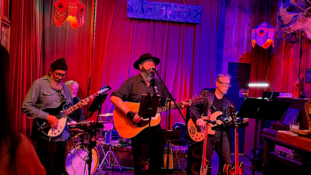 a four-person band plays on a small stage with red curtains behind them at the Riptide bar in San Francisco