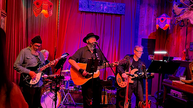 a four-person band plays on a small stage with red curtains behind them at the Riptide bar in San Francisco