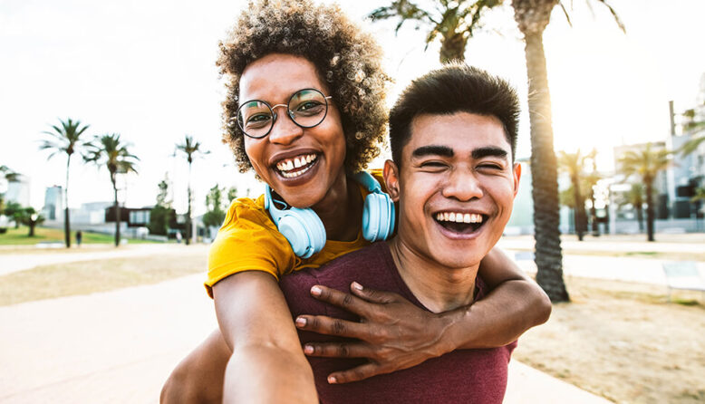 a young man giving a young woman a piggy back ride while she takes a selfie of the two of them