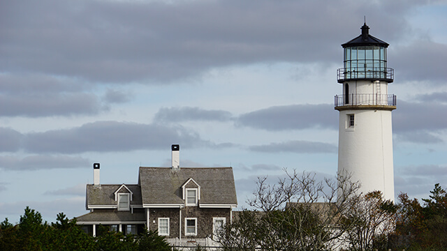 a tall white lighthouse sits beside a grey lighthouse station on Cape cod