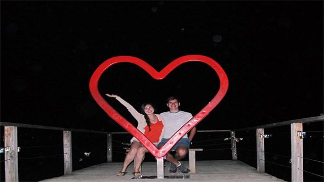 A couple posing with a heart art sculpture