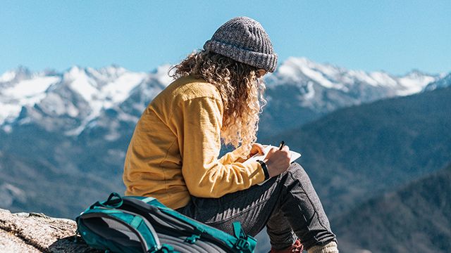 woman writing in a journal on top of a mountain