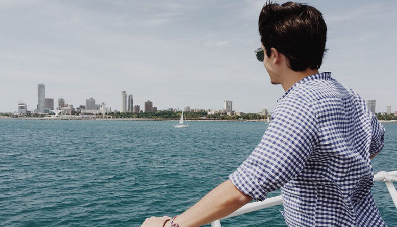 man looking over the railing of a ferry at the Milwaukee skyline