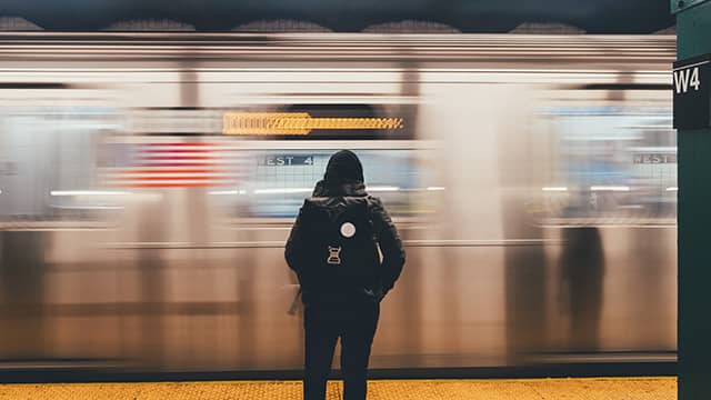 a New York City subway train passes as a woman waits on the platform