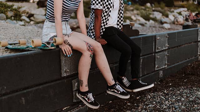 two skateboarders sit on a wall talking