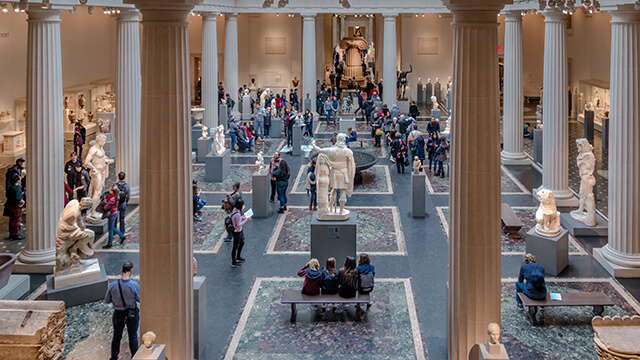 a large museum floor with marble columns, statues, and people admiring the exhibits