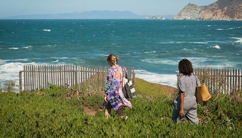 two women walk down a path to the beach