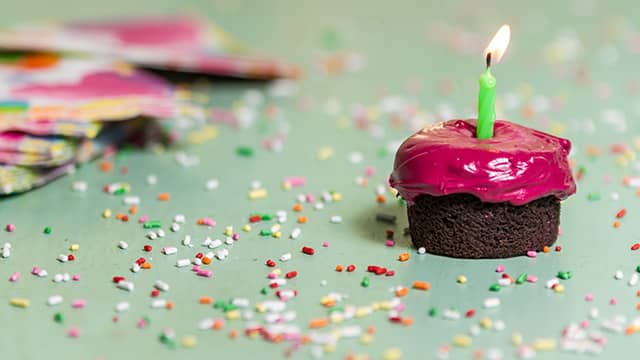 a chocolate cupcake with pink frosting and a green birthday candle