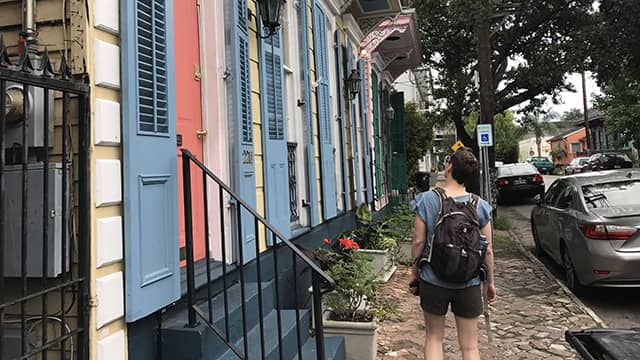 a woman walks down the sidewalk in a residential neighborhood in new orleans