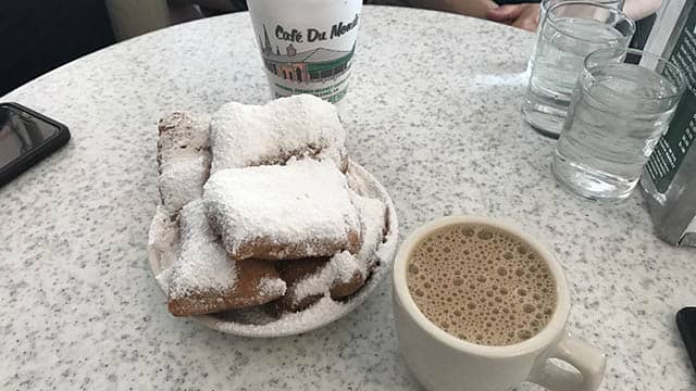 a cup of cofeee and a plate of beignets on a table
