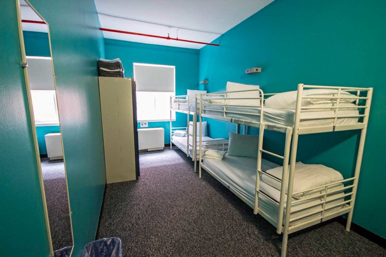 a small dorm room at HI New York City hostel with teal walls and two sets of bunk beds with crisp white linens.