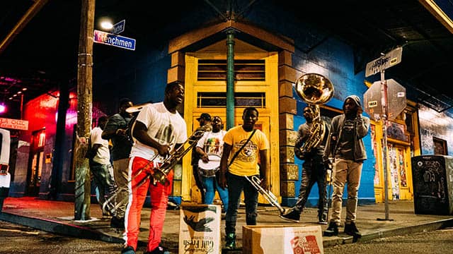 a group of mean play instruments on a street corner in front of a yellow building