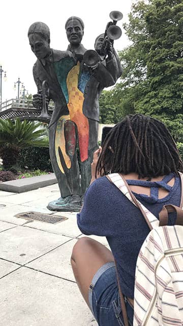a woman kneels down to take a photo of a colorful statue in New Orleans' Louis Armstrong Park