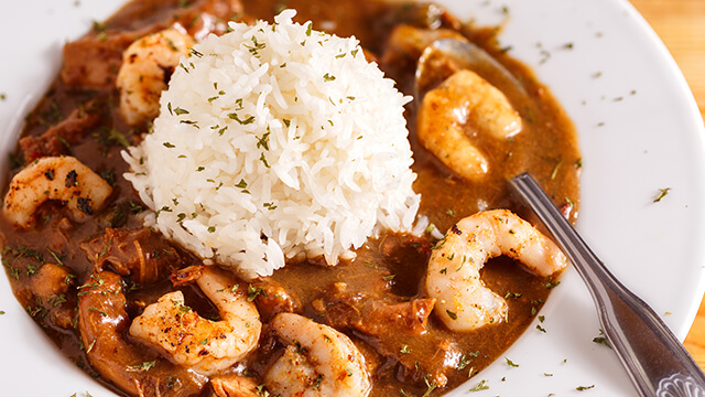 close up of a white bowl of gumbo with shrimp and a large scoop of white rice in the middle